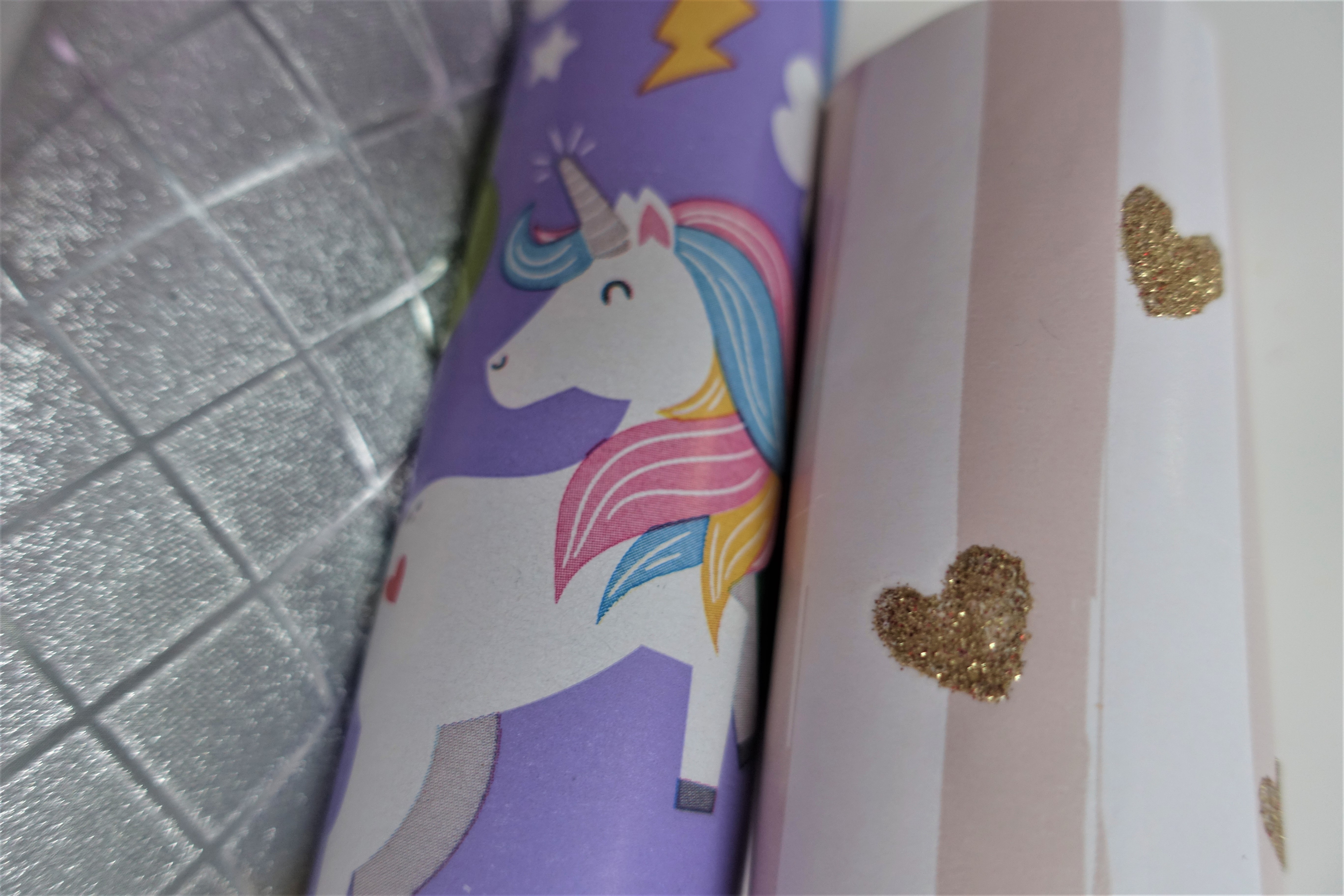 Two rolls of wrapping paper with golden hearts and unicorns each